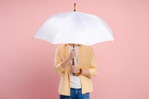 Young man hiding his face behind a white umbrella on a pink background photo