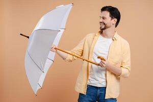 Happy man holding white umbrella smiling looking away on beige background photo