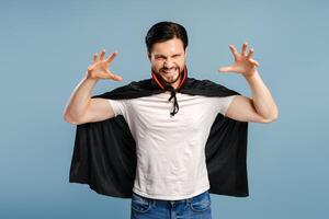 Man wearing vampire costume making scary face for halloween standing isolated on blue background photo