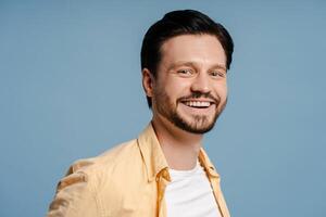 Cheerful young man with beard smiling and posing isolated on blue background photo