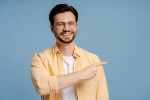 Cheerful man pointing aside while smiling on blue background photo