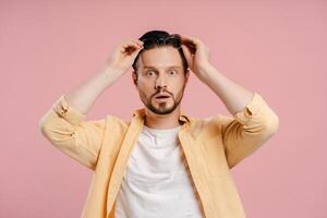 Shocked man adjusting glasses on pink background, looking at camera photo