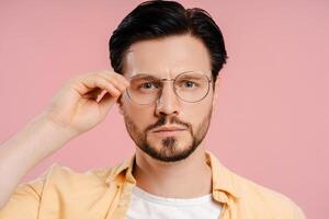 Serious man wearing stylish eyeglasses looking at camera posing on pink background photo
