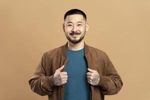Smiling asian man with tattoos showing clothes is posing in studio photo