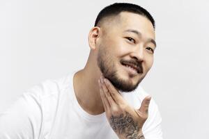 Smiling asian man touching his beard on white background photo
