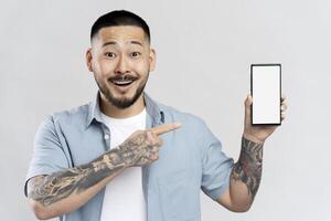 Excited asian man with tattoos showing smartphone with empty screen for mobile app advertisement photo