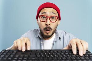 Shocked asian man wearing red glasses and beanie typing on keyboard photo