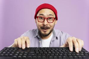 Excited asian man using a keyboard with a purple background photo