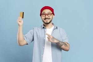 Smiling man showing credit card and pointing at it on blue background photo