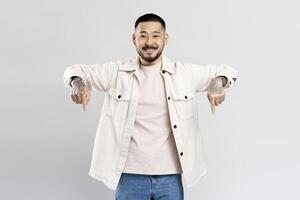 Smiling asian man with tattoos pointing down with both hands on a white background photo