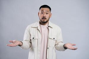 Confused asian man shrugging with open palms posing in studio photo