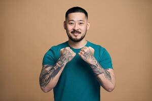 Young tattooed man showing fists on brown background photo