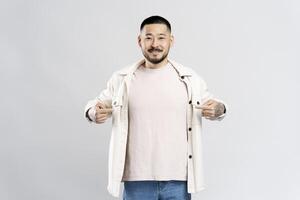 Smiling asian man pointing fingers at his t shirt on white background photo
