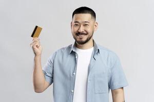 Smiling young man showing credit card on grey background photo