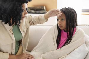 Mother checking daughter's forehead temperature on sofa photo