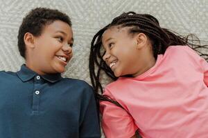 Two happy children lying down on carpet smiling at each other photo