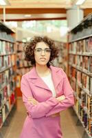 Confident librarian posing with crossed arms in library photo