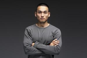 Serious young man is crossing his arms on a dark background photo