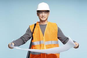 Smiling asian construction worker holding blueprints on blue background photo