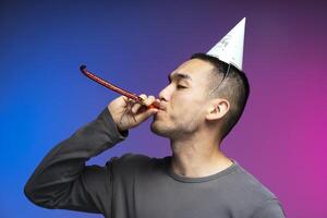 Young man celebrating with party blower and hat on colorful background photo