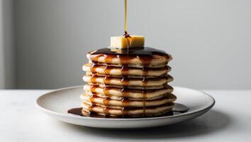 A stack of pancakes with syrup and butter being poured over them photo