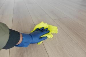A person is diligently cleaning the floor using a bright yellow cloth and wearing blue gloves photo