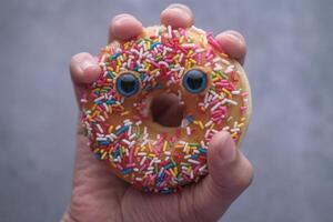 Hand Holding a Delightful, Fun Donut Covered in Colorful Sprinkles and Adorned with Googly Eyes photo