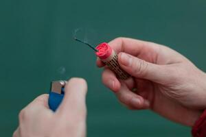 Man Lighting Up Firecracker in his Hand Against the Blue Background Using Gas Lighter photo