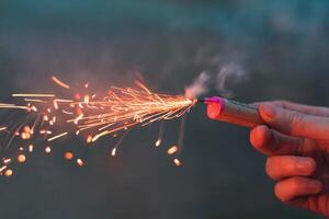 Young Man Lighting Up Firecracker in his Hand Outdoors in Evening. Guy Getting Ready for New Year Fun with Fireworks or Pyrotechnic Products - CloseUp Shot photo