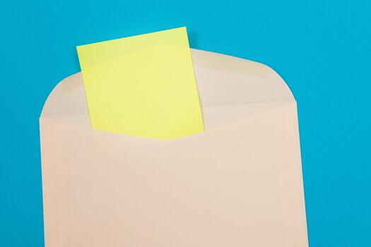 Beige Envelope with Blank Yellow Sheet of Paper Inside, Lying on Blue Background - Mock Up with Copy Space. Receiving Mail or Notice, Sending Postcard - Top View, Flat Lay photo