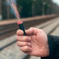 The Firecracker in a Hand. Man Holding a Burning Petard in His Hand. A Human with a Pyrotechnics that Burns with Sparks and Smoke Outdoors photo