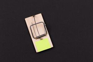 Blank Yellow Sheet of Paper in Wooden Mousetrap - Template. Small Memo Paper in Mouse Trap on Black Background photo