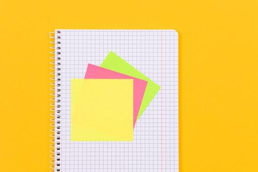 A Notepad with Sticky Notes Lying on Yellow Table - Blank Template. Top View, Flat Lay photo