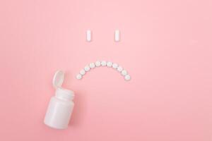 Pharma Harm. Sad Smiley Face Made from White Pills, Lying on Pink Backgrond. Global Pharmaceutical Industry and Medicinal Products photo