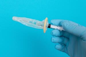 Safe Vaccine, Anti Vaccination Concept - Syringe in a Condom Holds in a Hand with Medical Glove. Mistrust of Vaccination. Natural Immunity. Skepticism About the Vaccine. Freedom and Human Rights photo
