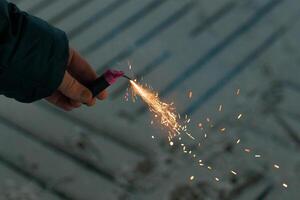 Burning Firecracker with Sparks. Guy Holding a Petard in a Hand. Loud and Dangerous New Year's Entertainment. Hooliganism with Pyrotechnics. Noise of Firecrackers in Public Places photo