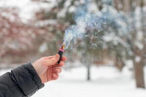 Burning Firecracker in a Hand. Guy Holding a Petard Outdoors in Winter at Daytime. Loud and Dangerous New Year's Entertainment. Hooliganism with Pyrotechnics. Noise of Firecrackers in Public Places photo
