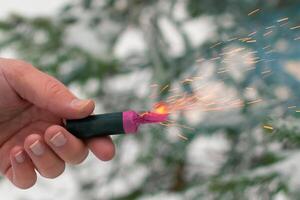 Burning Firecracker in a Hand. Guy Holding a Petard Outdoors in Winter at Daytime. Loud and Dangerous New Year's Entertainment. Hooliganism with Pyrotechnics. Noise of Firecrackers in Public Places photo