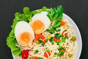 Beautiful Noodle Dish with Green Pea, Carrot, Eggs, Red Hot Pepper and Greens on Black Background. Instant Noodles with Vegetables photo