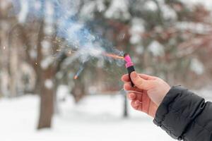 Burning Firecracker in a Hand. Guy Holding a Petard Outdoors in Winter at Daytime. Loud and Dangerous New Year's Entertainment. Hooliganism with Pyrotechnics. Noise of Firecrackers in Public Places photo