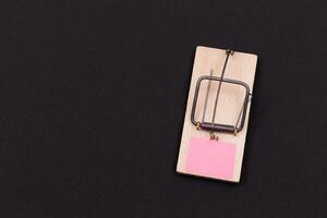 Blank Pink Sheet of Paper in Wooden Mousetrap - Template. Small Memo Paper in Mouse Trap on Black Background photo