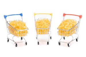Uncooked Fusilli Pasta in Three Small Shopping Carts Isolated on White Background. A Crisis. Buying Cheap Food. Classic Dry Spiral Macaroni. Italian Culture and Cuisine. Raw Pasta - Isolation photo