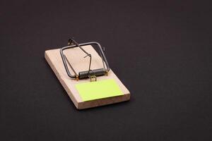 Blank Yellow Sheet of Paper in Wooden Mousetrap - Template. Small Memo Paper in Mouse Trap on Black Background photo