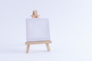 Wooden Easel Miniature with Blank White Square Canvas for Artists and Painters - Mockup. Mini Wooden Stand with Clean Artboard on White Background, Copy Space photo