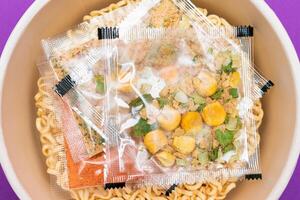 Opened Package with Uncooked Instant Noodles on Violet Background. Raw Pasta. Dry Asian Fast Food. Quick Lunch photo
