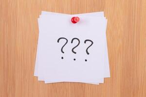 White Sticky Notes with Three Question Marks Pinned to the Wooden Message Board. To Do List Reminder in the Office. Memo Note at Work photo