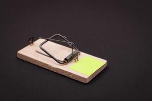 Blank Yellow Sheet of Paper in Wooden Mousetrap - Template. Small Memo Paper in Mouse Trap on Black Background photo