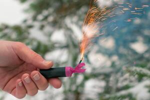 Burning Firecracker in a Hand. Guy Holding a Petard Outdoors in Winter at Daytime. Loud and Dangerous New Year's Entertainment. Hooliganism with Pyrotechnics. Noise of Firecrackers in Public Places photo