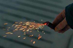 Burning Firecracker with Sparks. Guy Holding a Petard in a Hand. Loud and Dangerous New Year's Entertainment. Hooliganism with Pyrotechnics. Noise of Firecrackers in Public Places photo