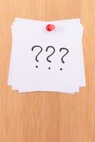 White Sticky Notes with Three Question Marks Pinned to the Wooden Message Board. To Do List Reminder in the Office. Memo Note at Work photo